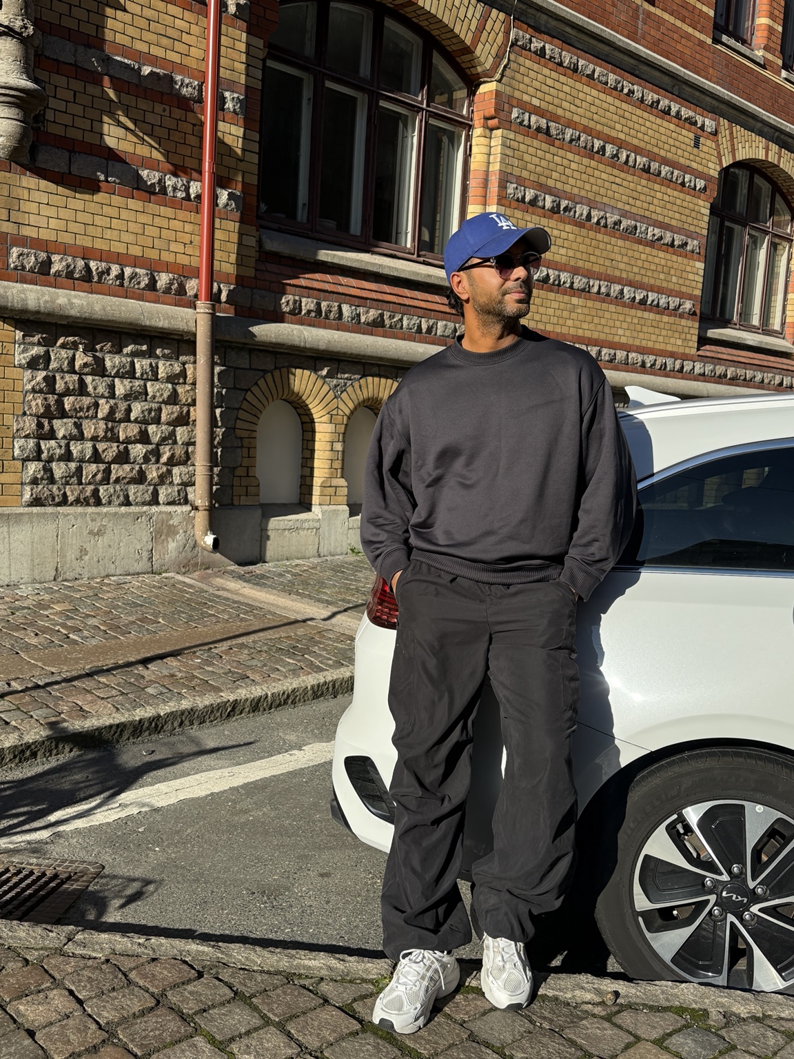 Merano med blå keps framför en tegelbyggnad